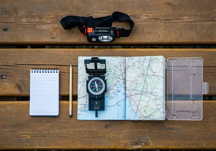 A flat lay of analog navigation tools, including a compass, topographic map, and other essential gear for hikers.