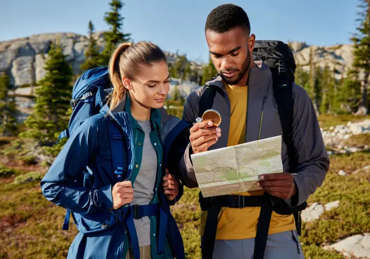 Diverse male and female hikers demonstrating navigation with a map and compass and adjusting clothing for thermoregulation in a rugged mountain environment, highlighting skills for ultralight backpacking.