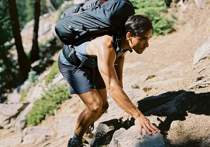 A male hiker with a weighted pack powers uphill on a rocky trail, demonstrating physical readiness and endurance for thru-hiking.