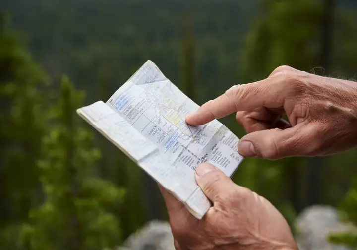 A hiker's hands holding a field guide or map, representing the practical application of the Seven Leave No Trace Principles.