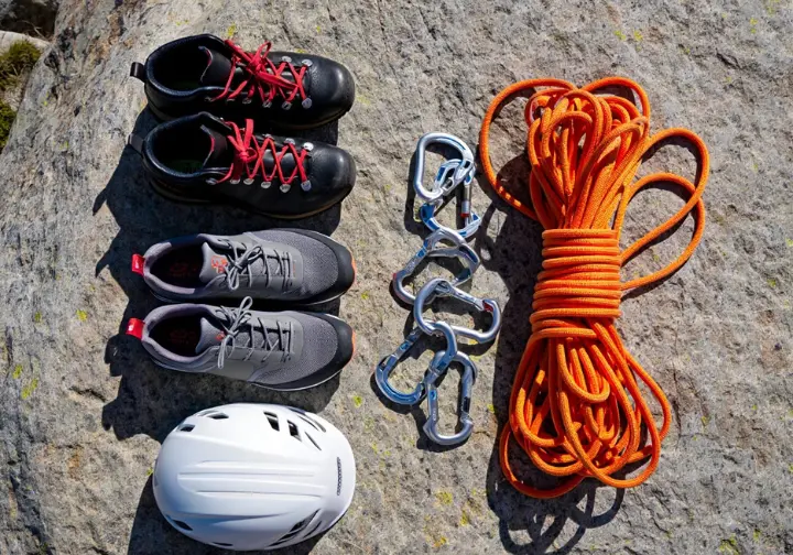 A flat lay of scrambling gear, including boots, approach shoes, and a helmet, representing a class-by-class toolkit for alpine scrambling.