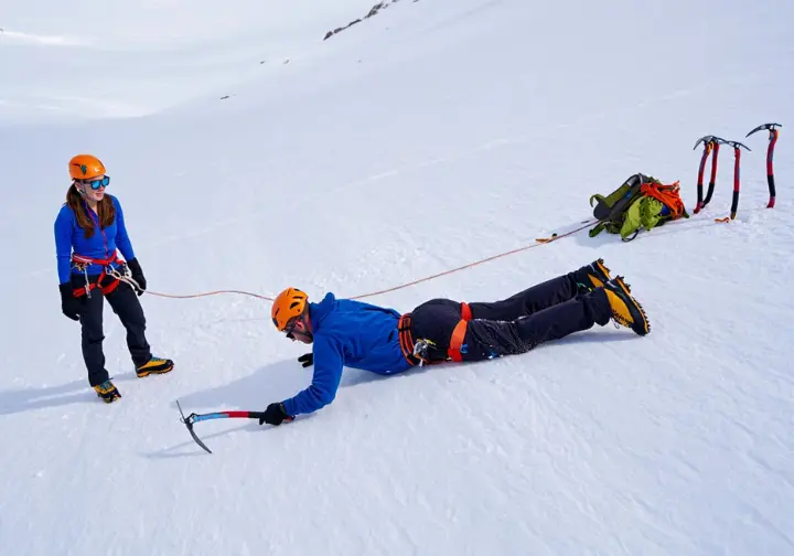 Two hikers practicing self-arrest on a gentle snow slope, demonstrating the importance of practice and avoiding pitfalls for effective fall stopping.