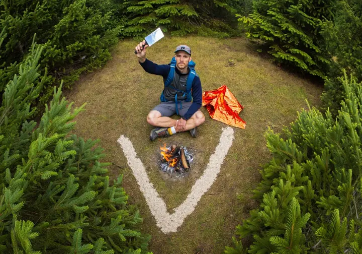 A lost hiker uses ground signals and a signal mirror to attract rescuers in a forest clearing.