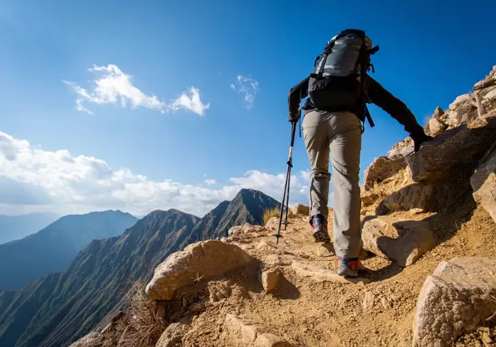 A hiker utilizing the rest-step technique to ascend a steep, rocky mountain path, symbolizing effective energy management and adaptation to challenging trail conditions.