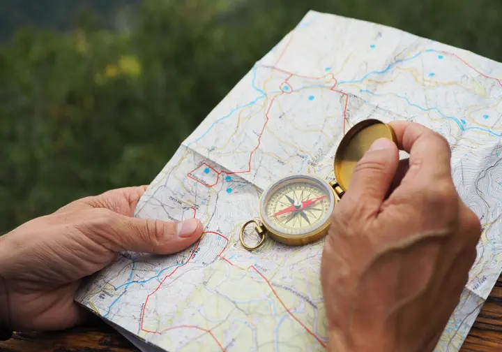 Hands holding a topographic map and compass, symbolizing mastery of navigation for uncovering hidden hiking trails.