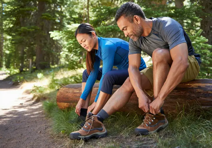 Hikers resting on a log, removing shoes to air out feet as part of proactive on-trail foot care.