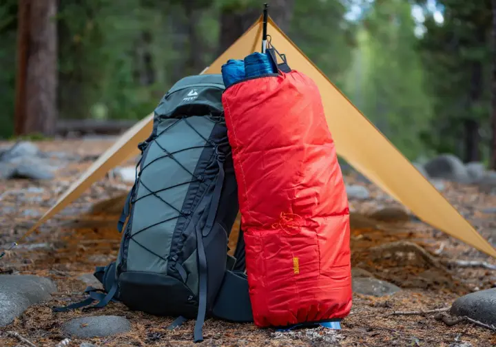 A minimalist tarp, a lightweight quilt, and an ultralight backpack are laid out on natural ground, representing the "Big Three" in strategic ultralight gear selection.