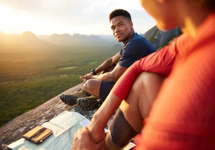 A thoughtful male hiker sitting on a rock, looking out over a vast wilderness, symbolizing the brain as the most important survival tool beyond the physical first-aid kit.