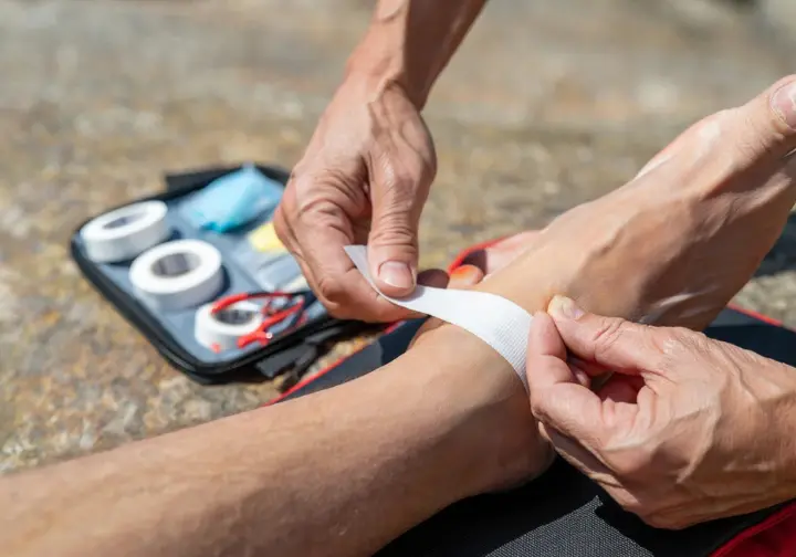 Hands applying tape to a heel with a blister kit, demonstrating trailside blister treatment and first-aid.