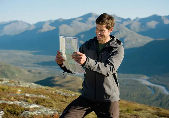 A hiker actively orienting a topographic map with a compass in a mountainous landscape, demonstrating real-world navigation techniques.