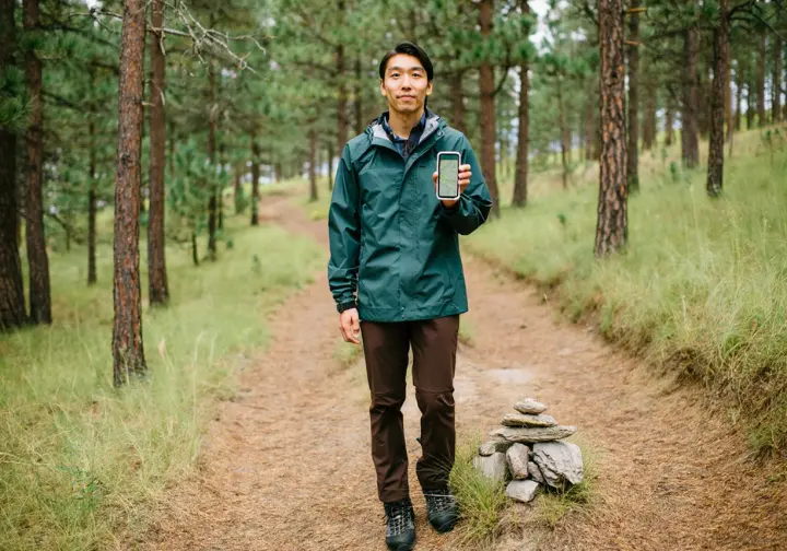 A hiker on a pristine trail holding a smartphone, representing the responsible use of digital tools and adherence to Leave No Trace principles in hiking.