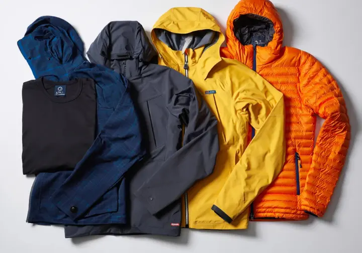 A flat lay showing a complete alpine layering system including baselayer, midlayer, softshell, hardshell, and puffy jacket for essential gear for alpine scrambling and easy mountaineering.
