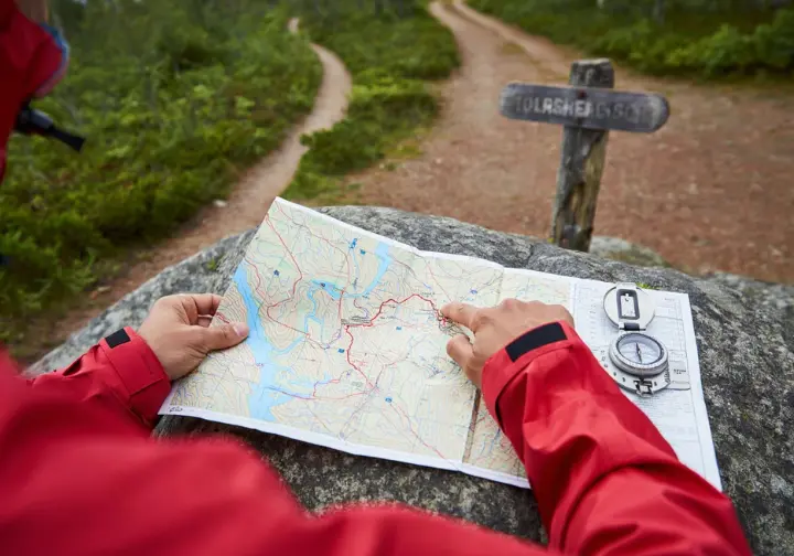 A hiker consulting a map with a compass on a rock, illustrating careful planning for a hike, avoiding common pitfalls, and respecting the trail.