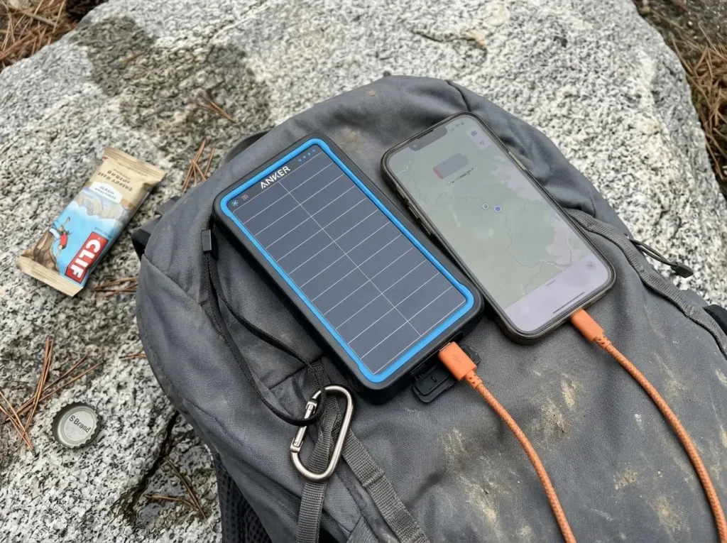 Phone charging from an Anker Solar power bank clipped to a pack on a long hike