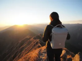 A hiker with a modern, lightweight backpacking gear setup watches the sunrise from a mountain peak, illustrating the benefits of choosing the right gear.