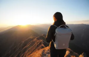 How to Choose Lightweight Backpacking Gear & Shed Lbs A hiker with a modern, lightweight backpacking gear setup watches the sunrise from a mountain peak, illustrating the benefits of choosing the right gear.
