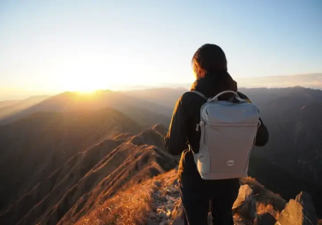 A hiker with a modern, lightweight backpacking gear setup watches the sunrise from a mountain peak, illustrating the benefits of choosing the right gear.