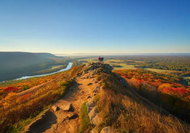 A stunning autumn view from a hiking trail overlook in Connecticut, with hikers looking out over colorful, rolling hills.