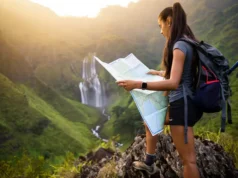 Find a Waterfall Hike: Maps, Gear & Pro Trail Tips A hiker with a backpack and map plans her route while looking out at a stunning, large waterfall in a mountain valley at sunset.