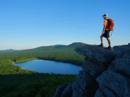 A hiker stands on the rocky summit of Chauncey Peak, looking at the panoramic view of Crescent Lake and Lamentation Mountain in Doctor Francis Giuffrida Park, Meriden, CT.