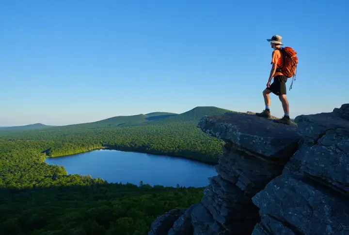 A hiker stands on the rocky summit of Chauncey Peak, looking at the panoramic view of Crescent Lake and Lamentation Mountain in Doctor Francis Giuffrida Park, Meriden, CT.