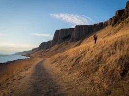 A wide, scenic view of a hiking trail in Palisades Interstate Park at sunset, showing the path along the Hudson River and up the cliffs.