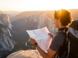 A hiker plans their route with a map while overlooking a vast California mountain landscape during a golden sunset, representing planning hiking trips in California.