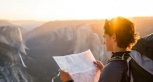 Hiking California: Plan the Ultimate Trip (Maps & Tips) A hiker plans their route with a map while overlooking a vast California mountain landscape during a golden sunset, representing planning hiking trips in California.