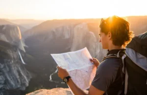 Hiking California: Plan the Ultimate Trip (Maps & Tips) A hiker plans their route with a map while overlooking a vast California mountain landscape during a golden sunset, representing planning hiking trips in California.