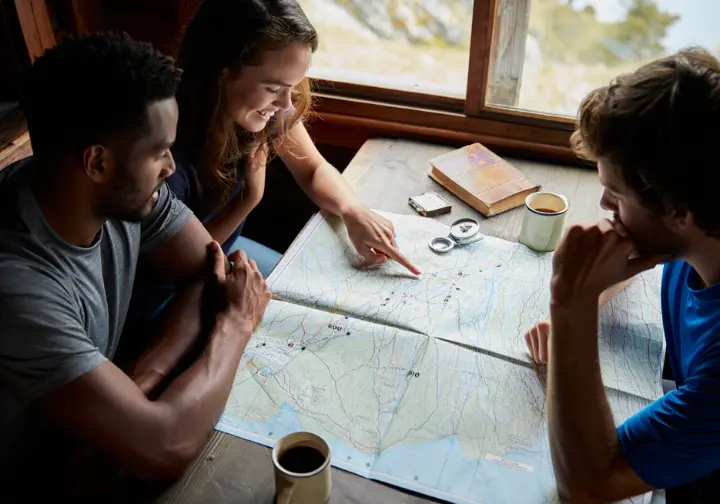 Two dedicated hikers study a large topographic map on a wooden table, carefully planning their perfect multi-day European trekking adventure.