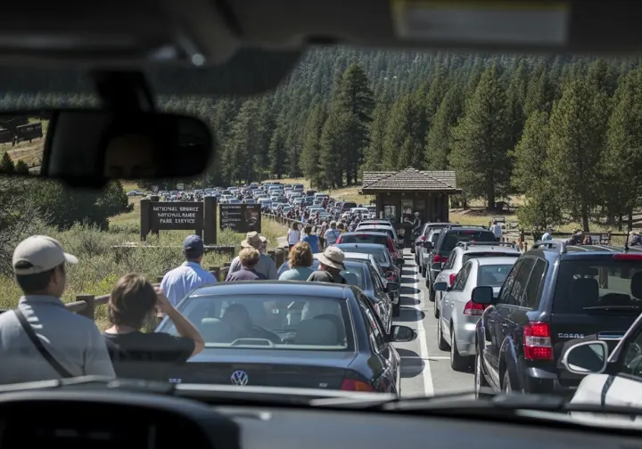 A long line of cars waits at a national park entrance station, illustrating the problem of park overcrowding and complicated access.