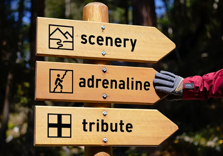 A hiker's hand touches a trail sign with three icons representing scenery, adrenaline, and tribute, to select a Storm King hike.