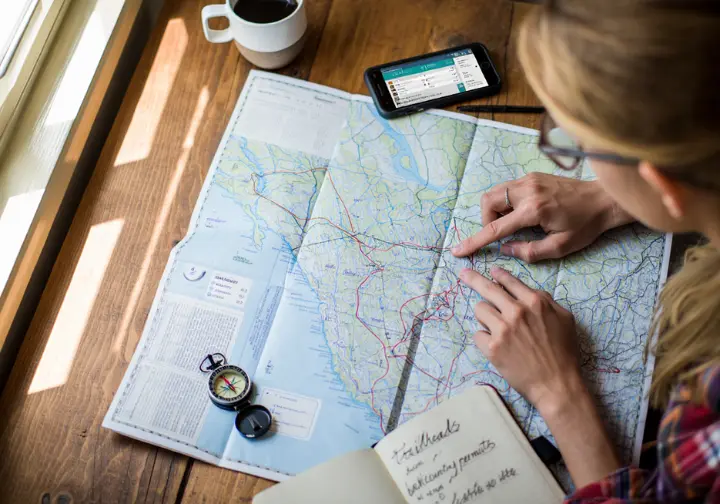 A hiker's hands tracing a route on a topographic map of Vancouver Island, surrounded by a compass and journal, representing a hiker's atlas.