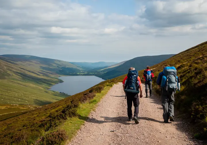 A small group of hikers on a multi-day journey walk along a trail overlooking a vast lake in the Scottish Highlands, representing Europe's best treks.