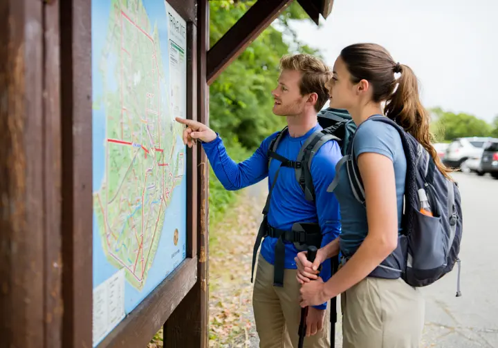 Two hikers planning their route by looking at a map at a trailhead kiosk in Palisades Interstate Park.