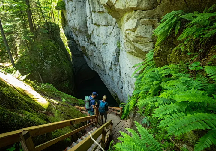Hikers stand at the entrance to the Sam's Point Ice Caves, looking down a wooden staircase into the dark, narrow rock crevice.