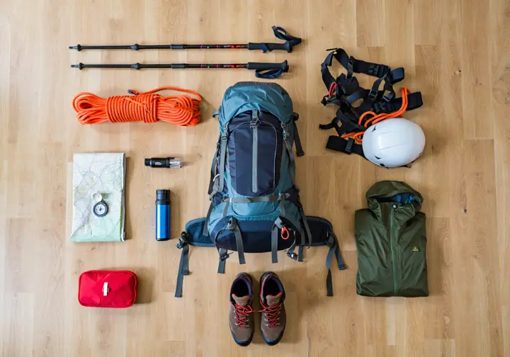 A top-down view of an essential hiker's toolkit for Europe, including a backpack, boots, poles, map, compass, and safety gear, all neatly arranged.