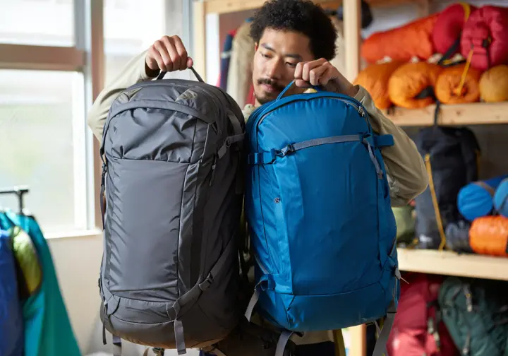 A hiker carefully compares two different ultralight backpacks as part of a gear selection guide for lightweight backpacking.
