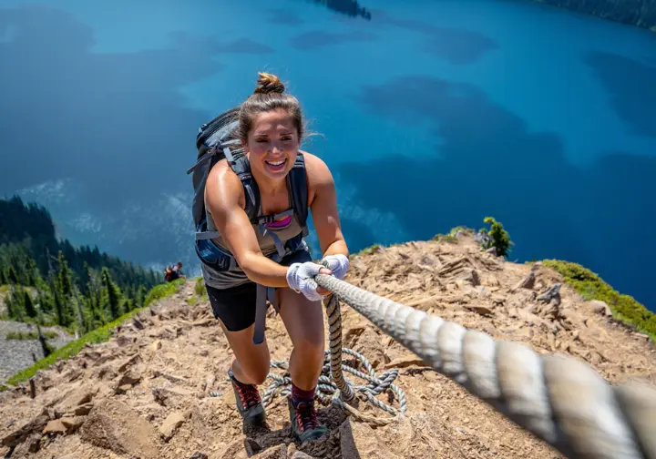A hiker uses the ropes for balance on the steep, exposed final ascent of the Mount Storm King hike above Lake Crescent, WA.