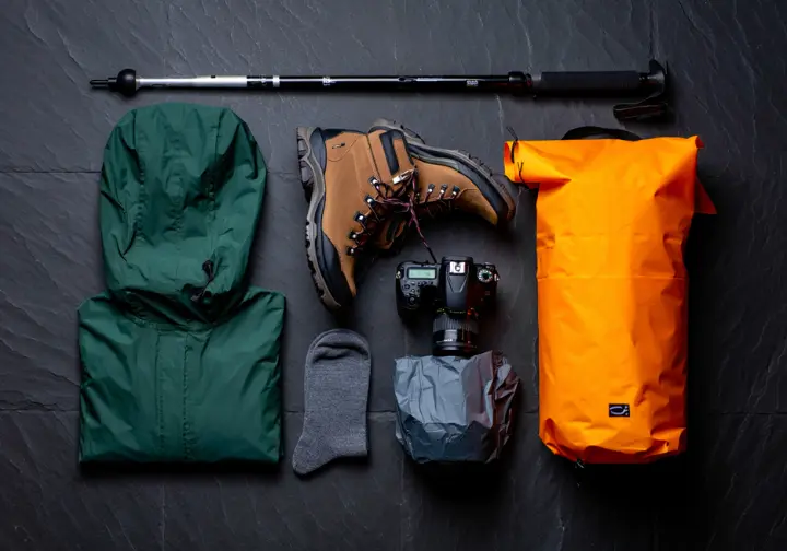 A flat lay of essential waterfall hiking gear, including waterproof boots, a rain jacket, trekking poles, and a dry bag.