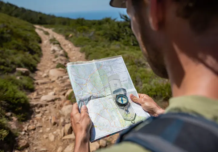 A hiker demonstrates advanced safety context by using a map and compass for navigation on a backcountry trail.