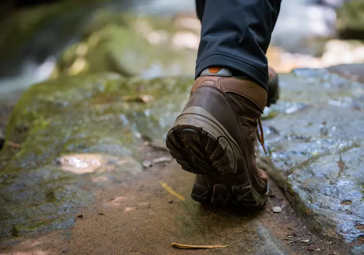 A close-up of a hiking boot placed safely away from a wet cliff edge, demonstrating trail safety and responsibility at Kaaterskill Falls.