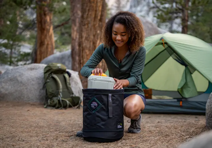 A responsible hiker stores food in a bear canister at a Sierra Nevada campsite, demonstrating safe and responsible hiking practices in California.