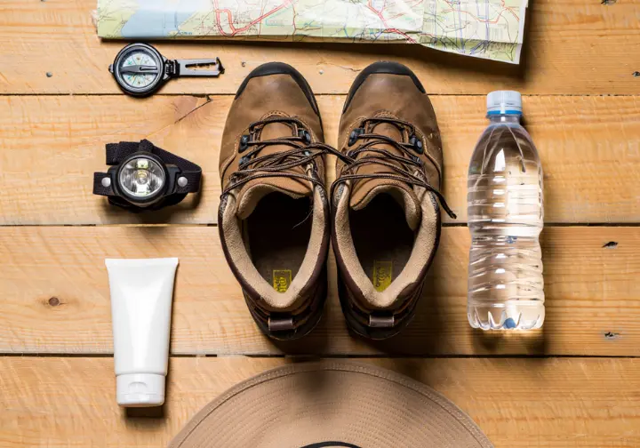 Essential hiking gear for Sam's Point, including hiking boots, a headlamp, a water bottle, and a map, arranged neatly on a wooden surface.