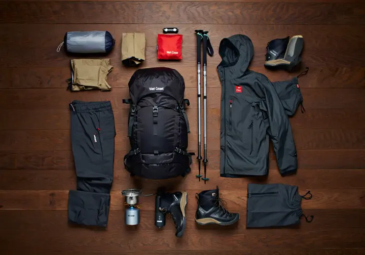 A complete hiking gear loadout for Vancouver Island, including a backpack, tent, and waterproof clothing, organized neatly on a wooden floor.