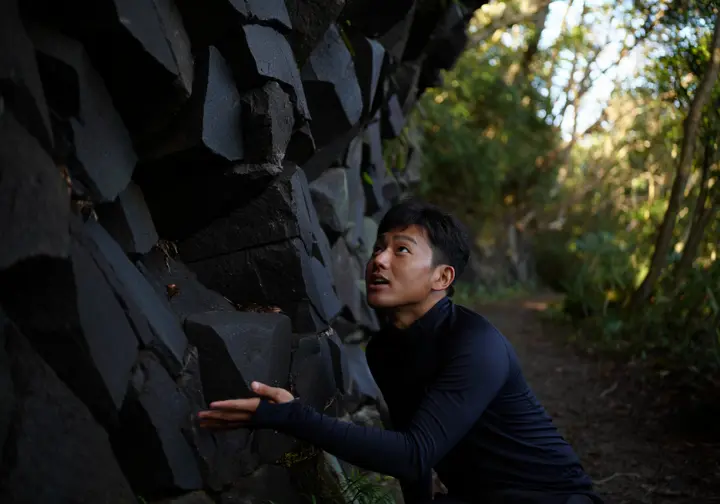 A hiker pauses to examine the unique volcanic traprock geology on a trail in Giuffrida Park, connecting the hike to the area's history.