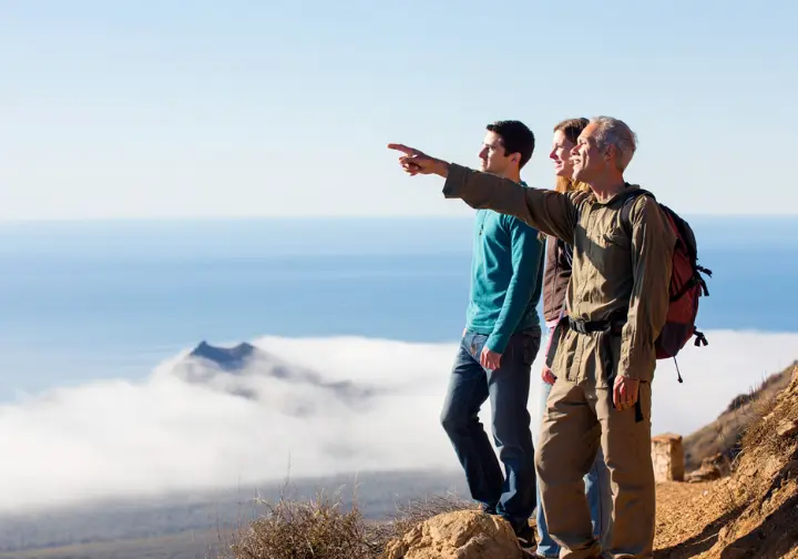 A hiking guide points out a landmark to a small group of hikers at a scenic overlook, representing guided hiking tours in California.
