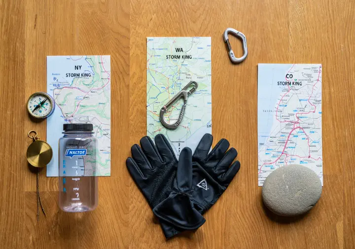 A flat lay photo comparing maps and essential gear for the three Storm King hikes in New York, Washington, and Colorado.