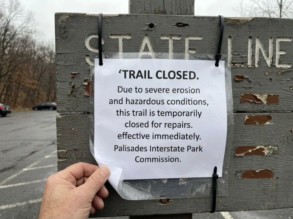 Trail closure notice zip-tied to a trailhead sign board at State Line Lookout in Palisades Interstate Park