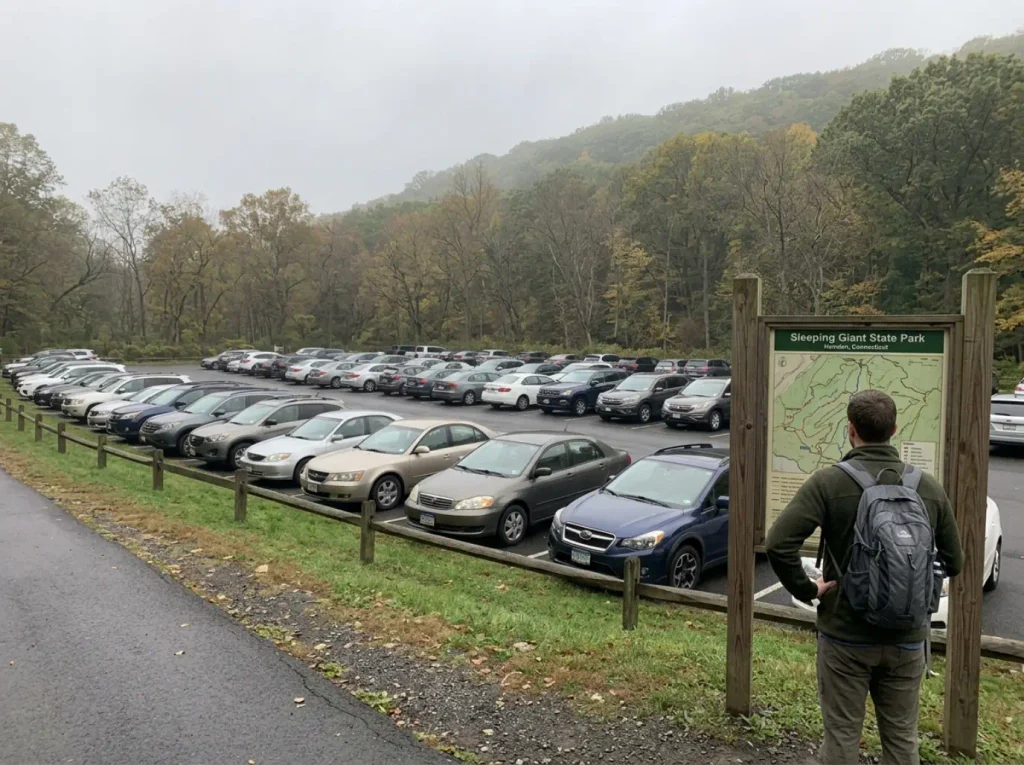 Full trailhead parking lot at a Connecticut state park on a weekend morning with cars along the edge.